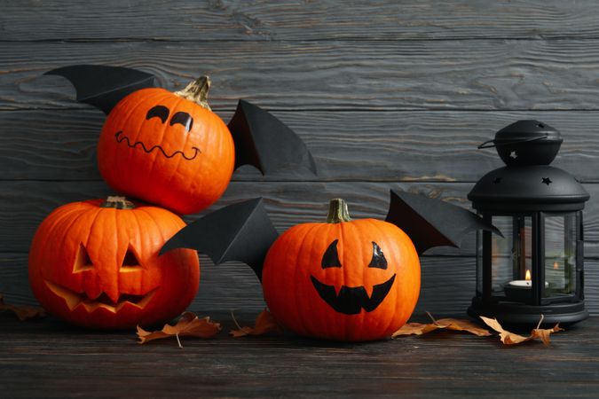 Lantern and pumpkins with wings on wooden background
