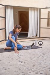 Smiling sportswoman using laptop on yoga mat