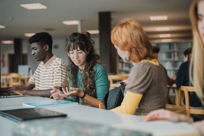 Young diverse groupmates talking in library during exam preparation