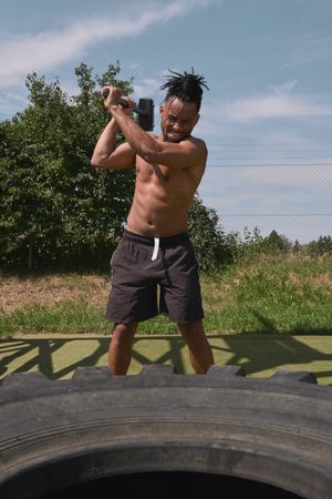 Muscular Black guy hammering tire in outdoor gym