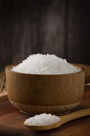 Coarse salt in bowl on wooden background.