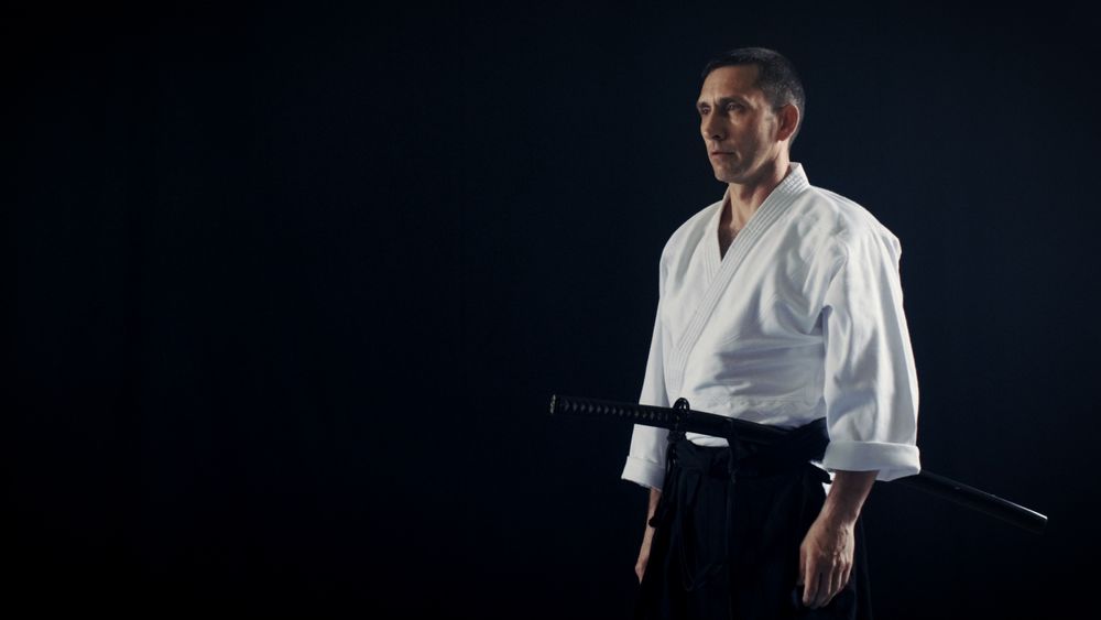 Portrait Shot of the Aikido Master Wearing Traditional Samurai Hakama Clothes Holds His Japanese Sword.