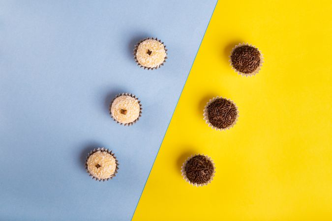 Top view of two rows of coconut & chocolate flavored truffles on blue yellow duo tone background