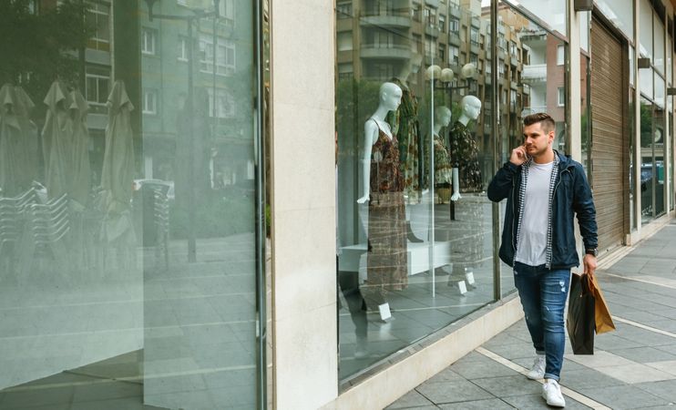 Man with shopping bags walking in front clothing store