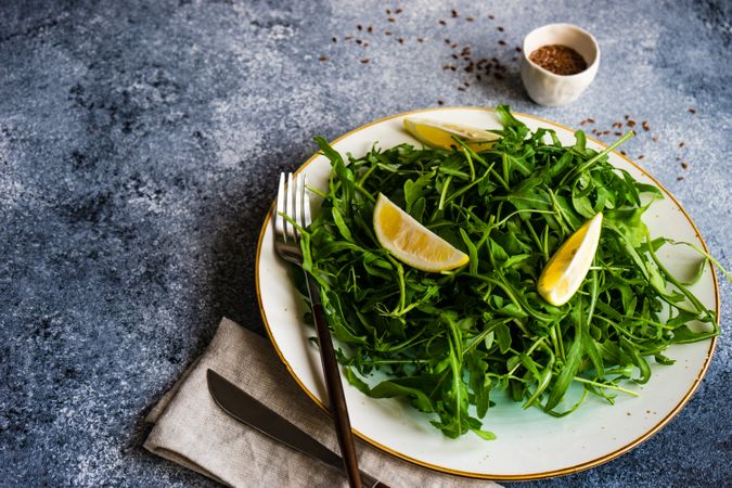 Healthy vegetable salad with organic arugula, lemon and flax seeds on stone background