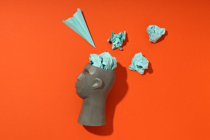 Side of grey bust of head on red background with paper airplane