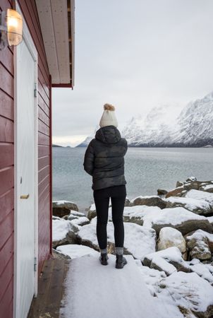 Solitary woman on rocky shore against tranquil lake and snowy mountains in cold day