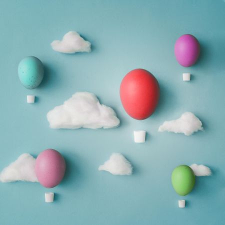 Hot air balloons made of decorated Easter eggs with cotton clouds on bright blue background