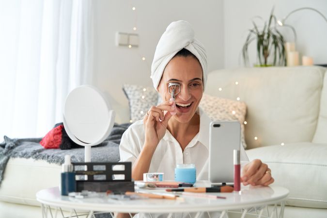 Cheerful female using eyelash curler and recording blog