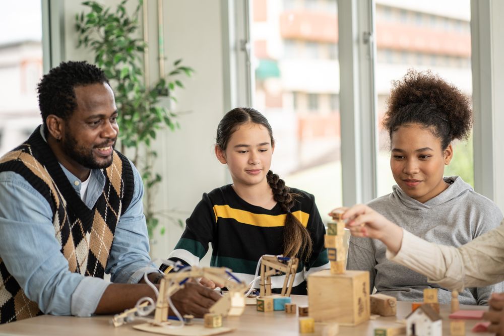 Male teacher watching his students build with wooden blocks in classroom