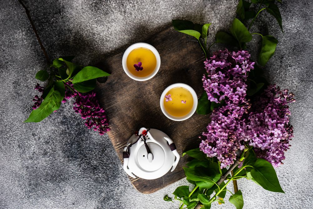 Top view of tray of teapot with filled cups with delicate tea and pink flowers