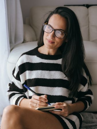 Woman writing in notebook near couch