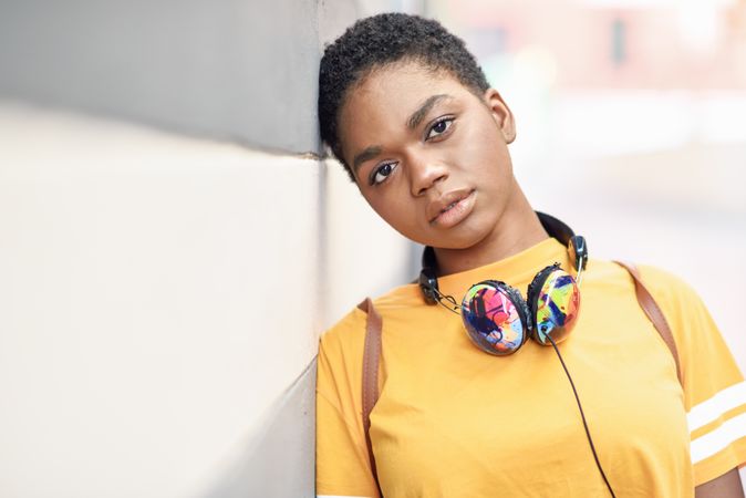 Serious Black woman with headphones leaning on grey striped wall