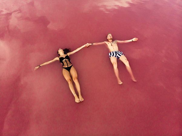 Idyllic couple in swimwear floating in pink water of lake