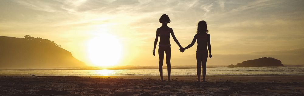 Silhouettes of two girls holding her hands in the beach at sunset