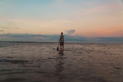 Man with paddle on surf board between waving water at sunset