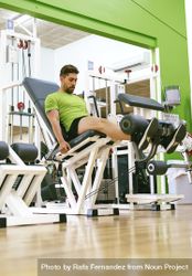 Side view of male in green t-shirt working out quads using gym equipment 5rr215