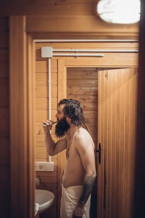 Bearded man brushing teeth in wooden house