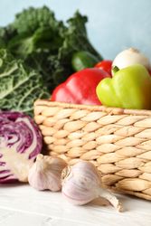 Wicker basket and vegetables on wooden background, close up