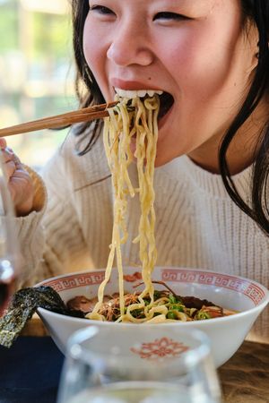 Young Asian female eating ramen in restaurant