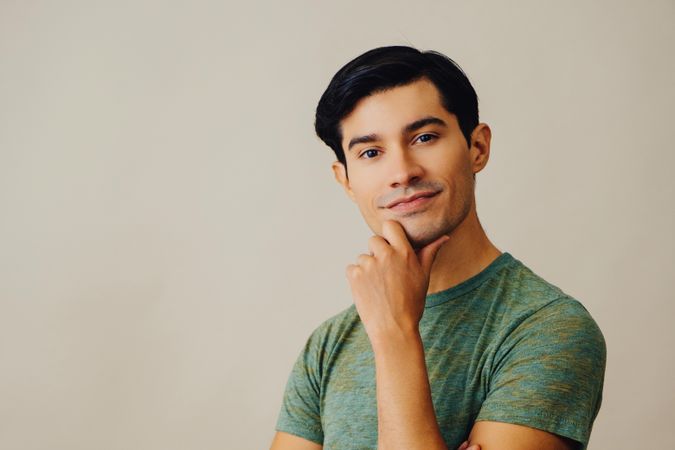 Curious Hispanic male holding his chin in neutral room