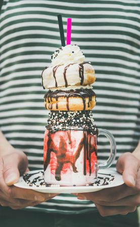 Man holding stacked donut milkshake with straws, whipped cream, and chocolate sprinkles
