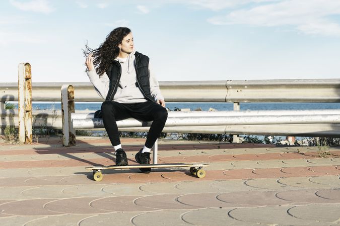 Teenage girl sitting on the coast with her feet on the longboard in front of the sea