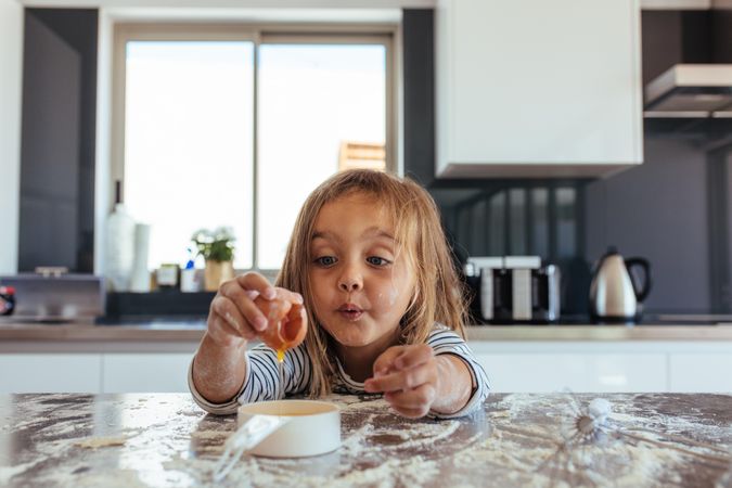 Cute little girl breaking an egg into a small pan over kitchen counter