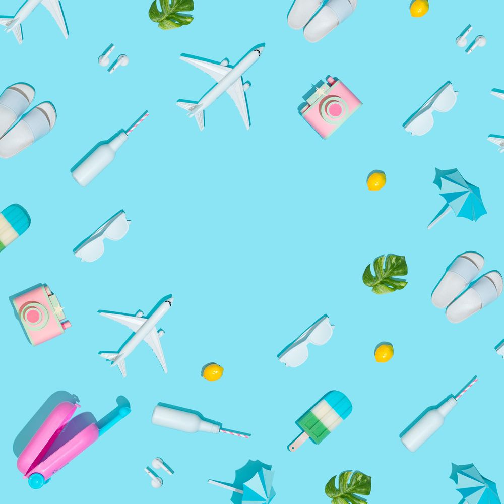 Suitcase and beach items, like camera, sunglasses, flip flops, on pastel blue background