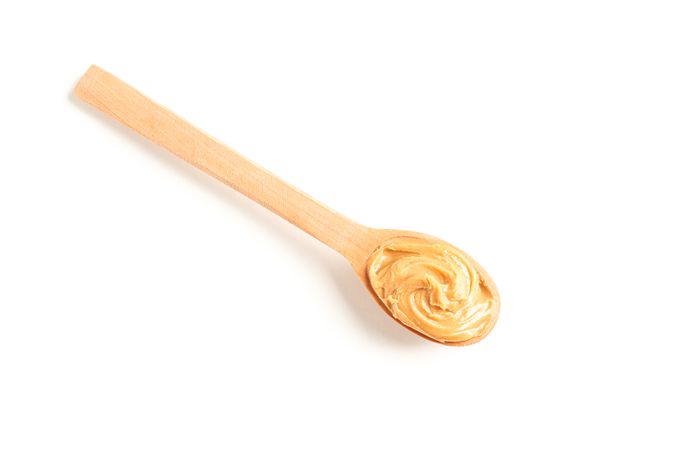 Creamy peanut butter in wooden spoon isolated on light background, top view. A traditional product of American cuisine