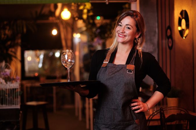 Cheerful waitress holding tray with wineglasses