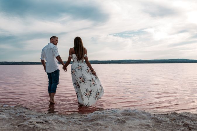 back view of adorable couple walking on an amazing beach with pink water