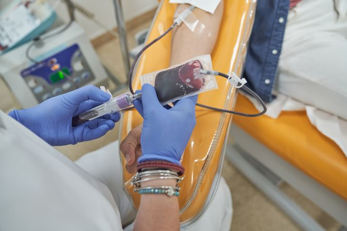 Crop doctor and female patient during blood donation in clinic