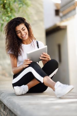 Content Arab woman looking down at her digital tablet while sitting outdoors, vertical