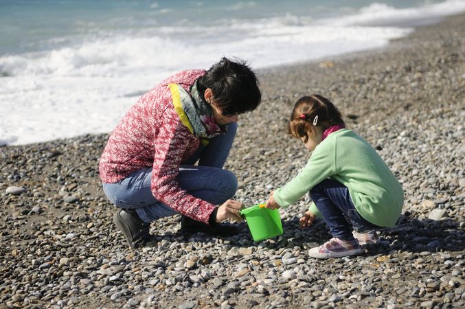 Woman and girl collecting rocks on a cold beach
