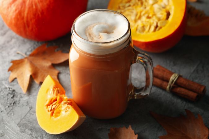 Composition with pumpkin latte, pumpkin, leaves and cinnamon on gray table