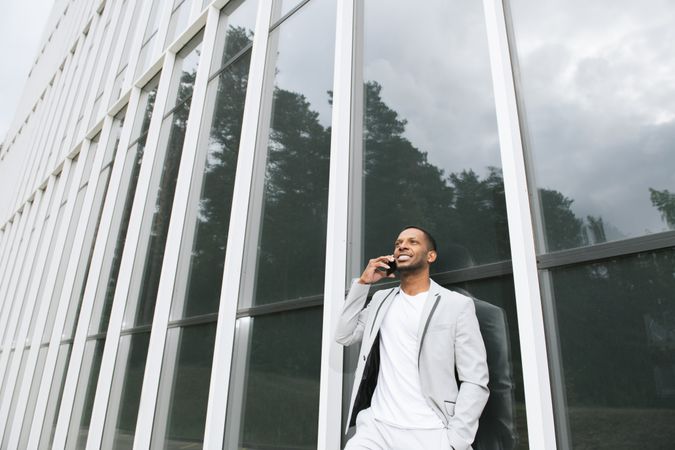 Elegant Black man talking smartphone leaning building
