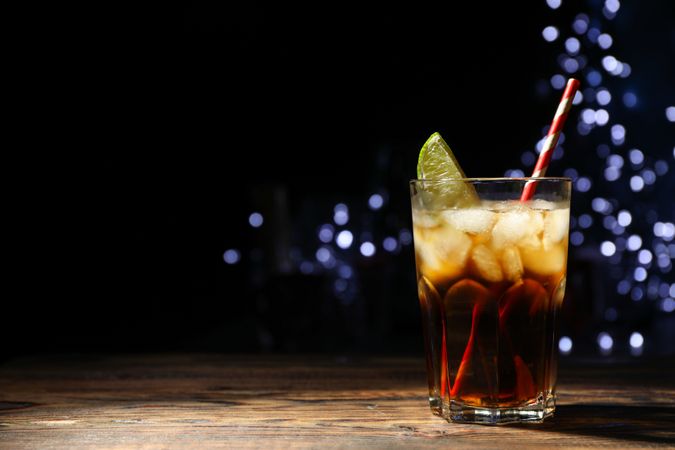 Glass with cola, lime slice and tubule against blurred lights background