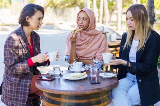 Three women chatting over coffee and baked goods on sunny outside table