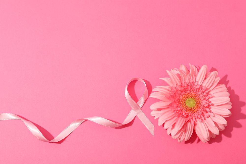 Pink awareness ribbon and gerbera on color background, space for text.