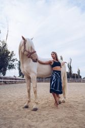 Graceful woman in skirt leaning on white horse side while dancing at paddock