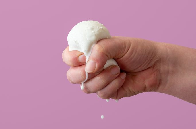Squeezing mozzarella ball in hand, close up on a purple background