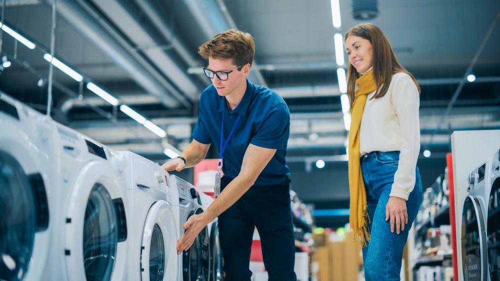 Portrait of a Retail Electronics Shop Consultant Assisting Young Female Customer in Selecting a Washing Machine For Her Home.