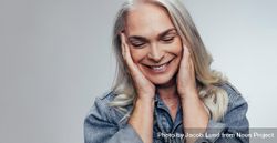 Woman with hands on face, smiling against grey background bYwwG5