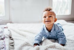 Baby boy lying on his belly looking up with a big smile