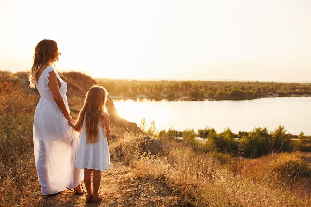 Woman and female child in summer dress enjoying the river view at dusk