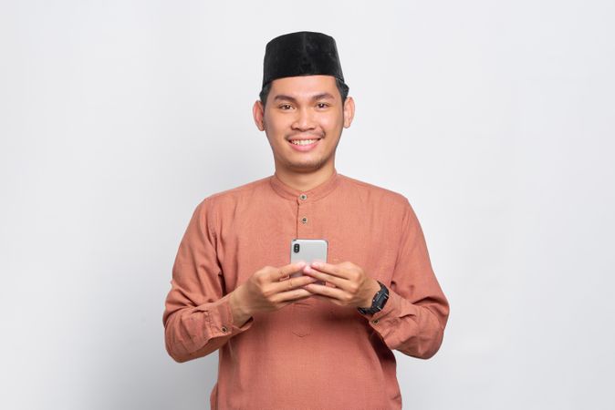 Muslim man in kufi hat smiling with smartphone