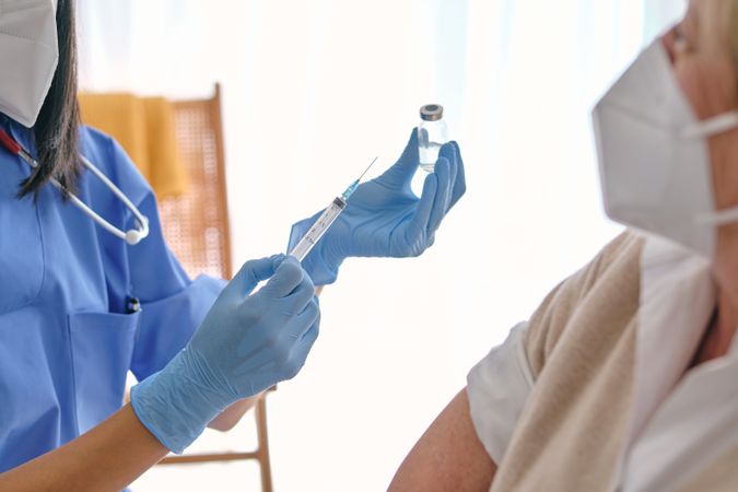 Crop physician with syringe and vaccine against female patient i
