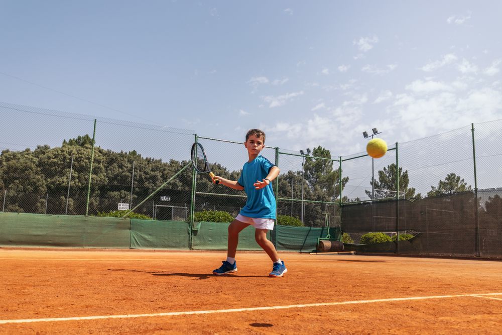 Little boy playing tennis on a dirt court