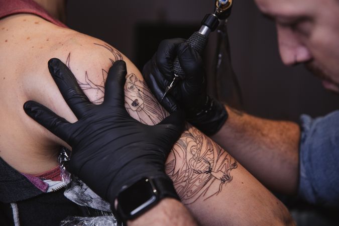 Master doing tattoo on forearm of male customer